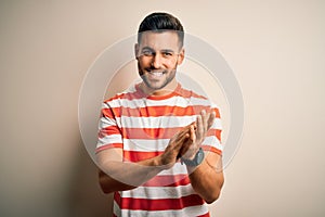 Young handsome man wearing casual striped t-shirt standing over isolated white background clapping and applauding happy and