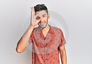 Young handsome man wearing casual summer clothes doing ok gesture with hand smiling, eye looking through fingers with happy face