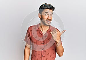 Young handsome man wearing casual summer clothes smiling with happy face looking and pointing to the side with thumb up