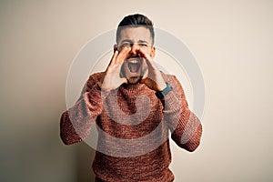 Young handsome man wearing casual sweater standing over isolated white background Shouting angry out loud with hands over mouth