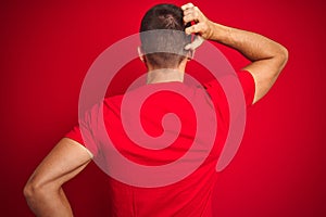 Young handsome man wearing casual t-shirt over red isolated background Backwards thinking about doubt with hand on head
