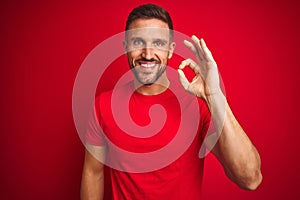 Young handsome man wearing casual t-shirt over red isolated background smiling positive doing ok sign with hand and fingers
