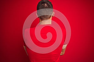 Young handsome man wearing casual t-shirt over red isolated background standing backwards looking away with crossed arms