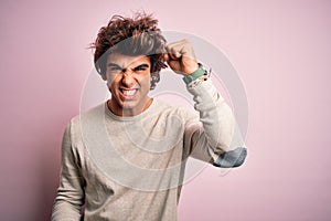 Young handsome man wearing casual t-shirt standing over isolated pink background angry and mad raising fist frustrated and furious