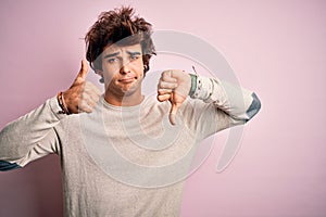 Young handsome man wearing casual t-shirt standing over isolated pink background Doing thumbs up and down, disagreement and