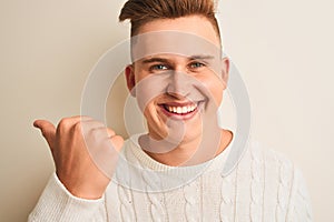 Young handsome man wearing casual t-shirt standing over isolated white background pointing and showing with thumb up to the side