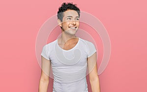 Young handsome man wearing casual white t shirt looking away to side with smile on face, natural expression