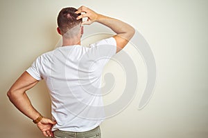 Young handsome man wearing casual white t-shirt over isolated background Backwards thinking about doubt with hand on head