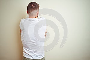 Young handsome man wearing casual white t-shirt over isolated background Hugging oneself happy and positive from backwards