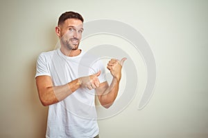 Young handsome man wearing casual white t-shirt over isolated background Pointing to the back behind with hand and thumbs up,