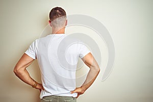 Young handsome man wearing casual white t-shirt over isolated background standing backwards looking away with arms on body