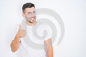 Young handsome man wearing casual white t-shirt over white isolated background doing happy thumbs up gesture with hand