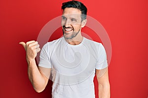 Young handsome man wearing casual white tshirt pointing thumb up to the side smiling happy with open mouth