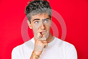 Young handsome man wearing casual white tshirt thinking concentrated about doubt with finger on chin and looking up wondering