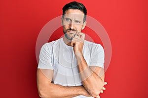 Young handsome man wearing casual white tshirt thinking concentrated about doubt with finger on chin and looking up wondering