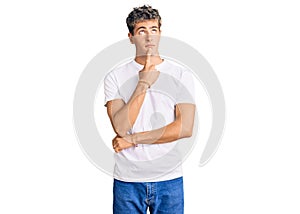 Young handsome man wearing casual white tshirt thinking concentrated about doubt with finger on chin and looking up wondering