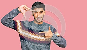 Young handsome man wearing casual winter sweater smiling making frame with hands and fingers with happy face