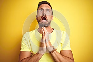 Young handsome man wearing casual yellow t-shirt over yellow isolated background begging and praying with hands together with hope