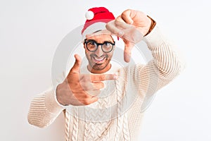 Young handsome man wearing christmas hat and glasses over isolated background smiling making frame with hands and fingers with