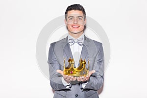 Young handsome man wearing with crown in hands suit looking at camera