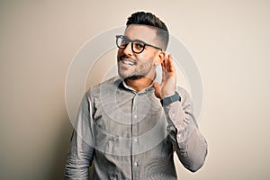 Young handsome man wearing elegant shirt and glasses over isolated white background smiling with hand over ear listening an