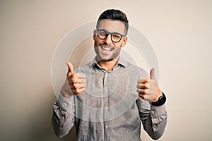 Young handsome man wearing elegant shirt and glasses over isolated white background success sign doing positive gesture with hand,