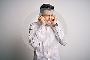Young handsome man wearing elegant shirt standing over isolated white background covering ears with fingers with annoyed