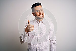 Young handsome man wearing elegant shirt standing over isolated white background doing happy thumbs up gesture with hand