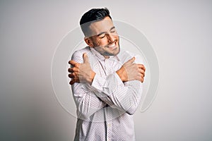 Young handsome man wearing elegant shirt standing over isolated white background Hugging oneself happy and positive, smiling