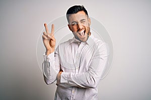 Young handsome man wearing elegant shirt standing over isolated white background smiling with happy face winking at the camera
