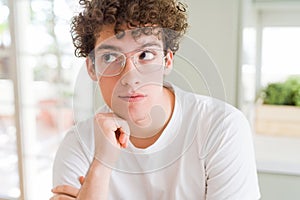 Young handsome man wearing glasses with hand on chin thinking about question, pensive expression