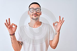 Young handsome man wearing glasses and standing over isolated background relax and smiling with eyes closed doing meditation