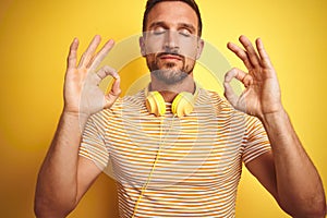 Young handsome man wearing headphones listening to music over yellow isolated background relax and smiling with eyes closed doing