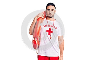 Young handsome man wearing lifeguard uniform holding float thinking attitude and sober expression looking self confident