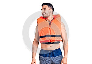Young handsome man wearing lifejacket looking away to side with smile on face, natural expression