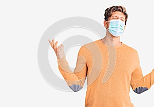 Young handsome man wearing medical mask crazy and mad shouting and yelling with aggressive expression and arms raised