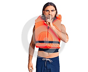 Young handsome man wearing nautical lifejacket asking to be quiet with finger on lips