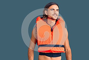 Young handsome man wearing nautical lifejacket looking away to side with smile on face, natural expression