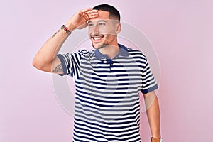 Young handsome man wearing nautical striped t-shirt over pink isolated background very happy and smiling looking far away with