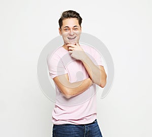 Young handsome man, wearing pink shirt looking at camera thoughtful holding hand on chin as thinkings