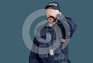 Young handsome man wearing police uniform covering eyes with hand, looking serious and sad