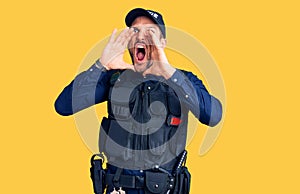 Young handsome man wearing police uniform shouting angry out loud with hands over mouth