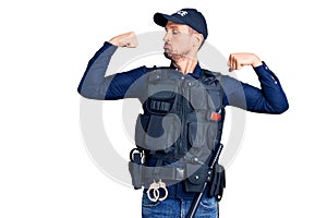 Young handsome man wearing police uniform showing arms muscles smiling proud