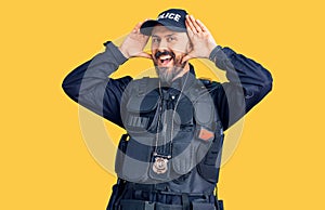 Young handsome man wearing police uniform smiling cheerful playing peek a boo with hands showing face