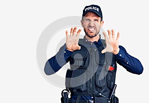 Young handsome man wearing police uniform smiling funny doing claw gesture as cat, aggressive and sexy expression