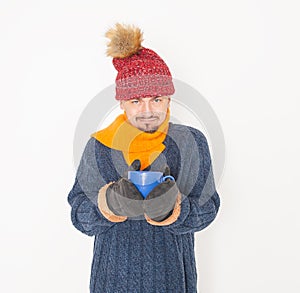 Young handsome man wearing in red hat and blue pullover feeling cold hold cup of hot drink on white background