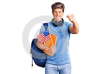 Young handsome man wearing student backpack and headphones holding book and america flag annoyed and frustrated shouting with