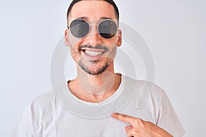 Young handsome man wearing sunglasses and casual t-shirt over isolated background with surprise face pointing finger to himself