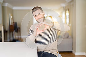 Young handsome man wearing a sweater at home smiling in love showing heart symbol and shape with hands
