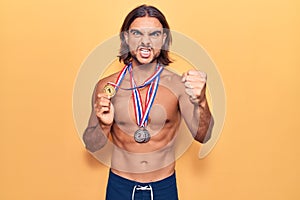 Young handsome man wearing swimwear and medals annoyed and frustrated shouting with anger, yelling crazy with anger and hand